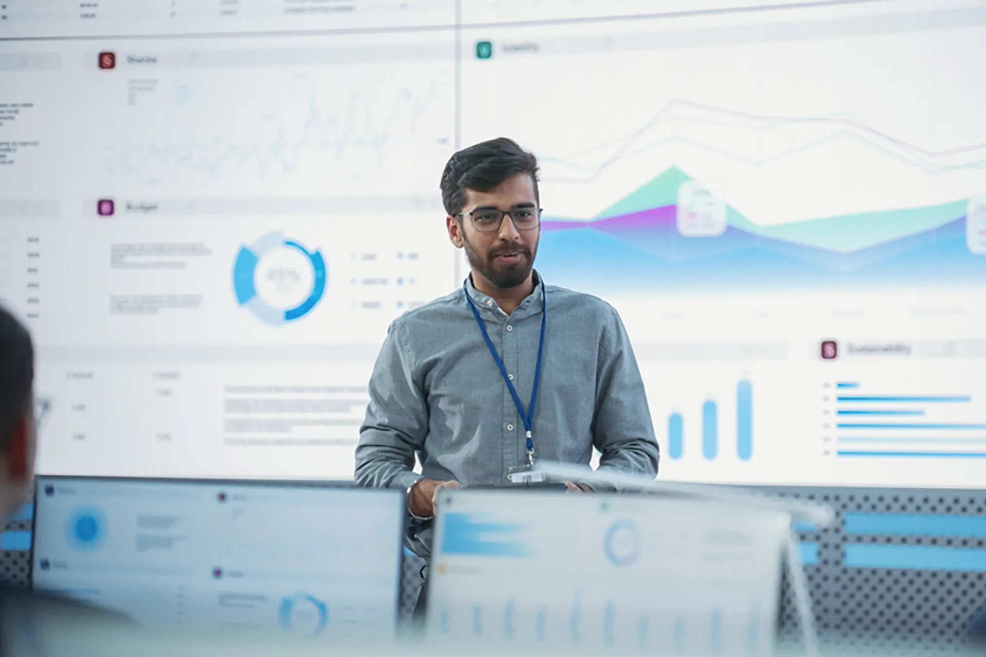 A young bearded man in glasses presenting data in front of a large screen.