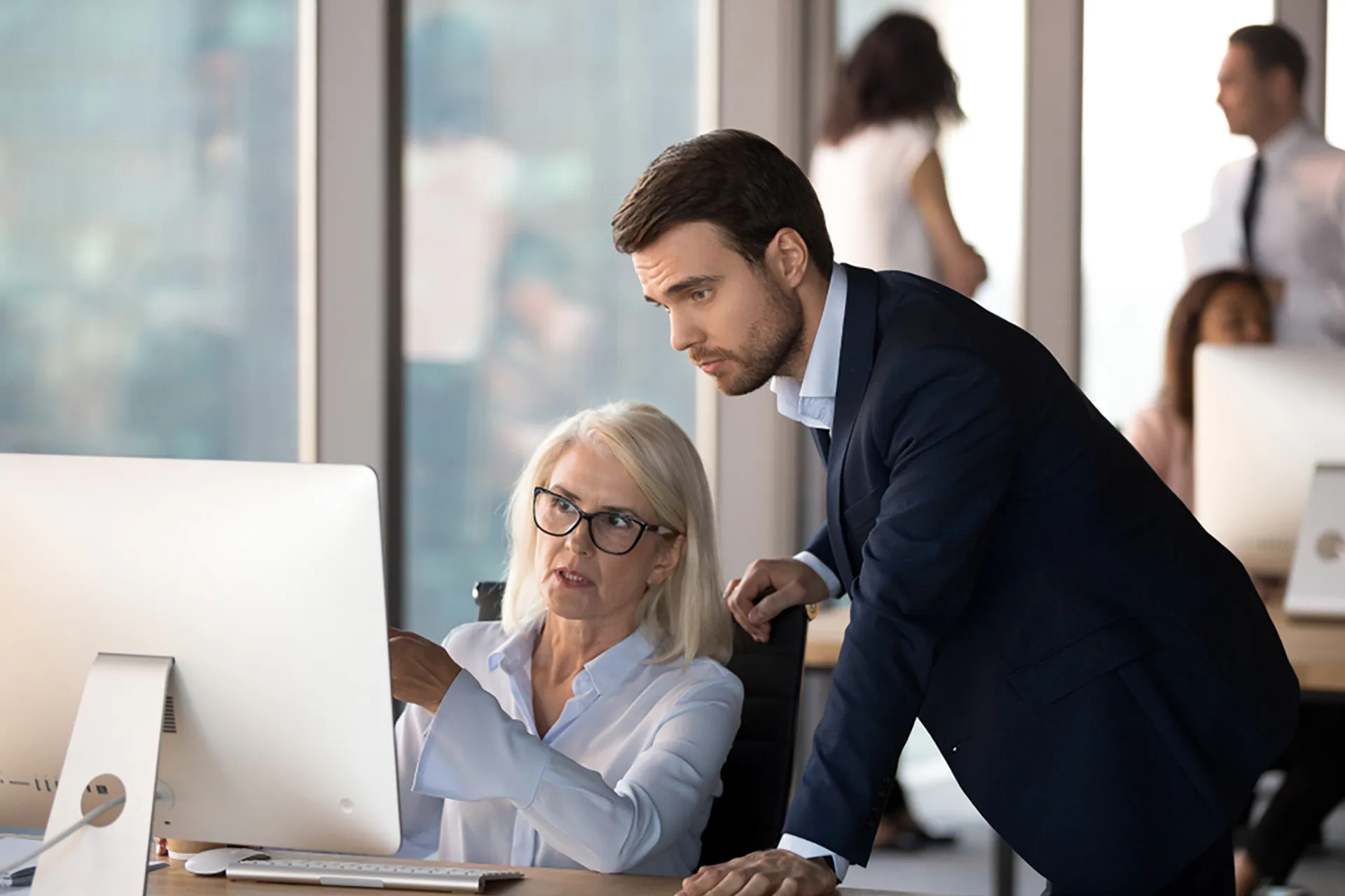 Male and female payroll professionals focused on a computer screen, in a modern office.