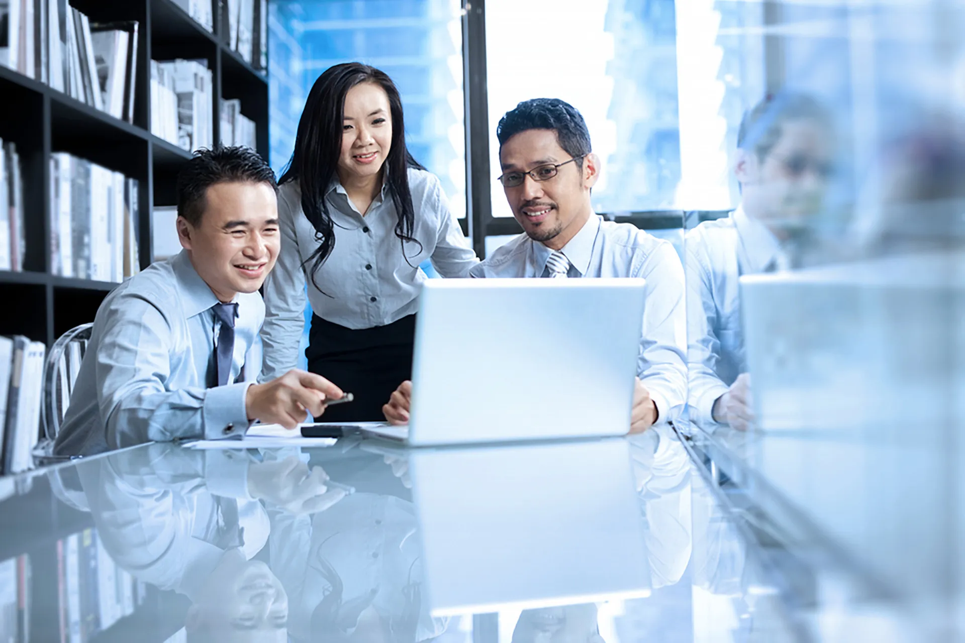  Three finance professionals collaborating at a table, focused on a laptop.