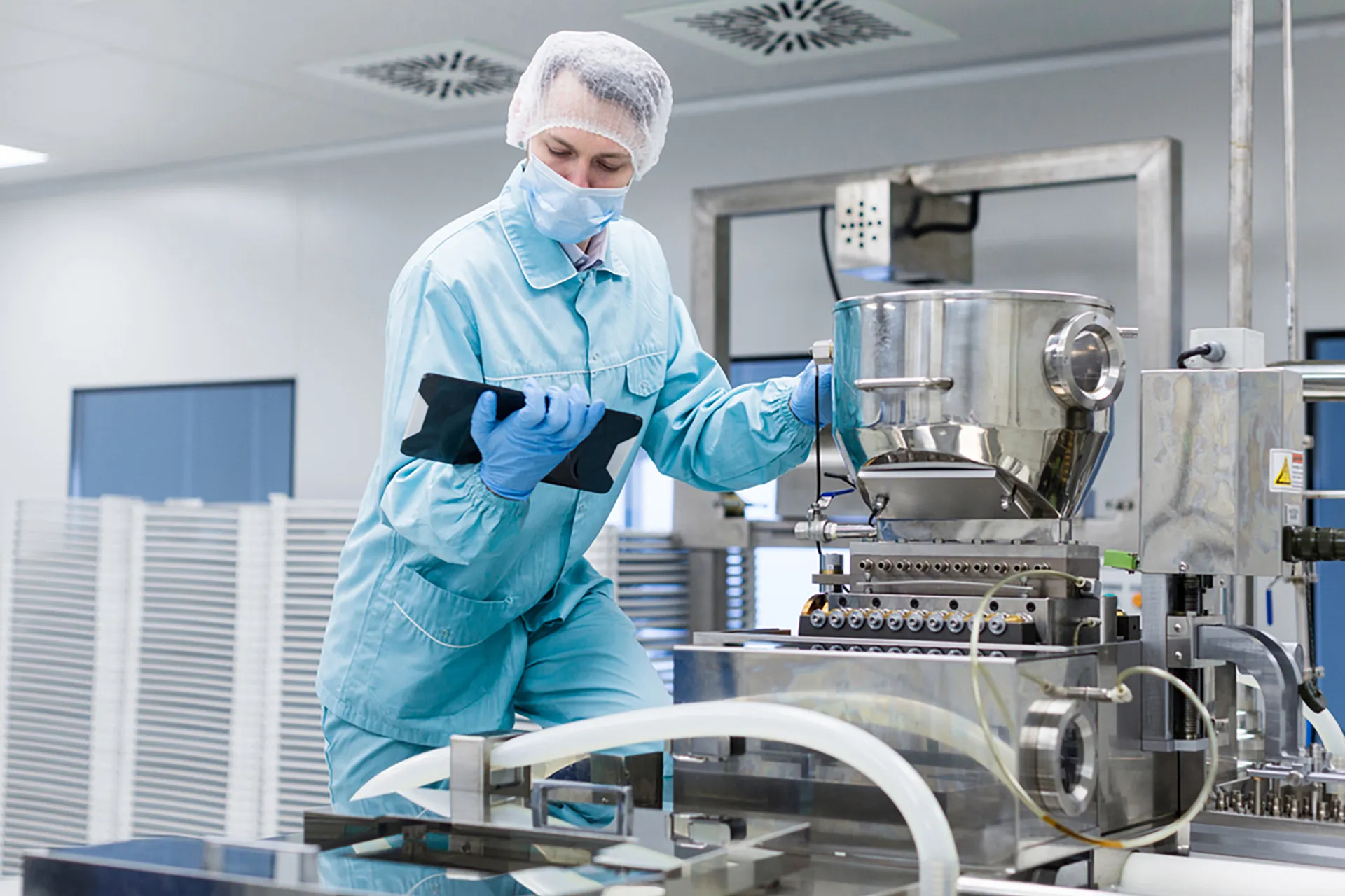 A man wearing a hair net and face mask conducts quality checks on modern machinery.