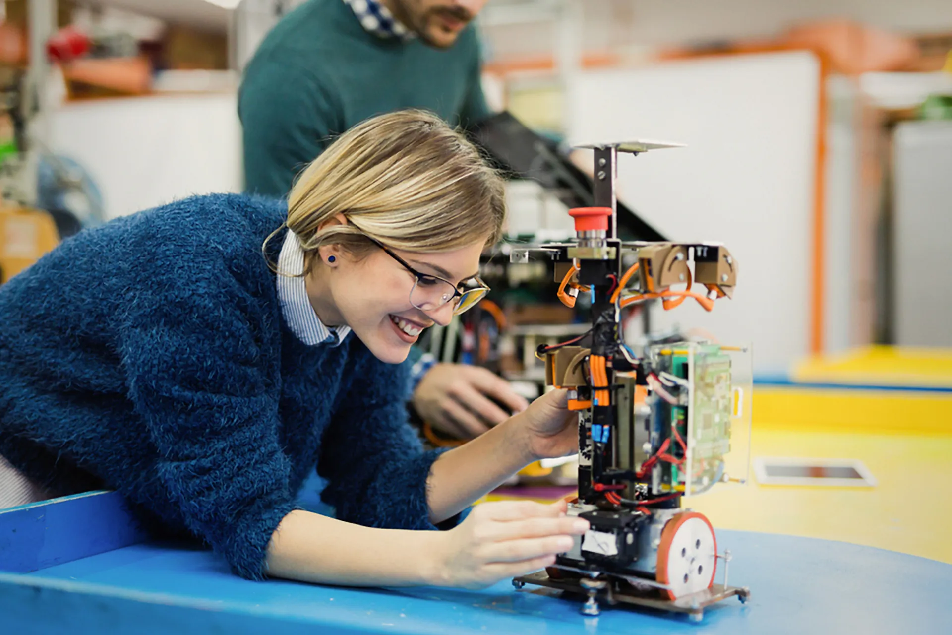 A man and young woman engrossed in their work, meticulously assembling a robot together in a workshop.