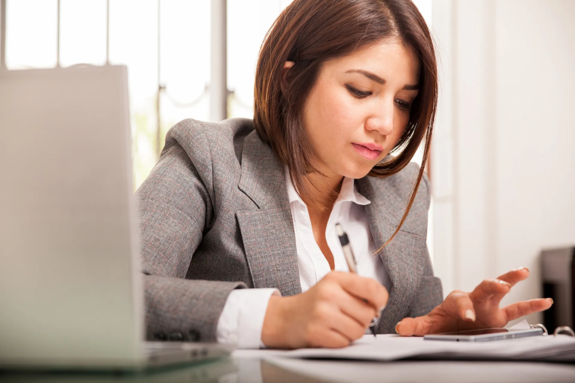  A professional woman in a suit reviewing paperwork and using a calculator.