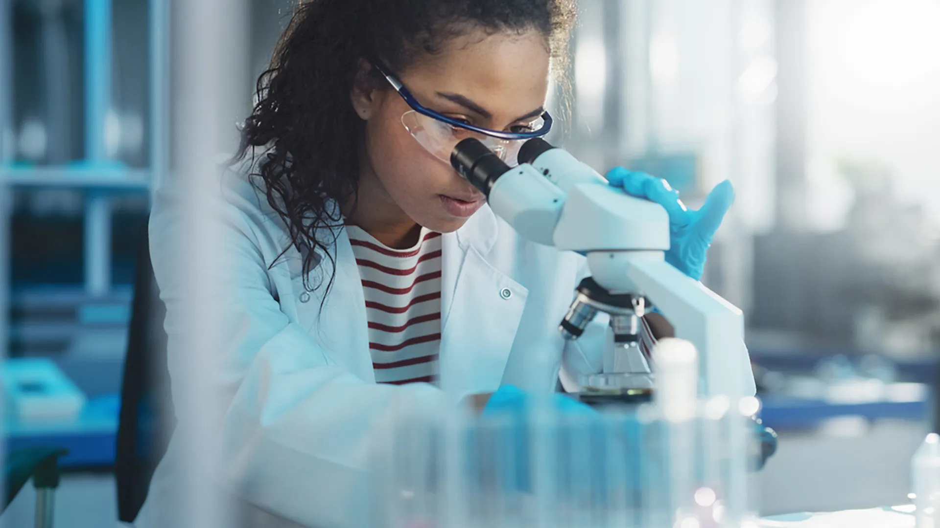 A woman wearing a lab coat carefully observing through a microscope.