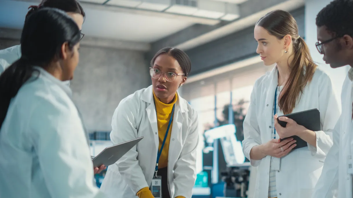 Group of diverse health and safety professionals in white lab coats and lanyards with serious expressions.