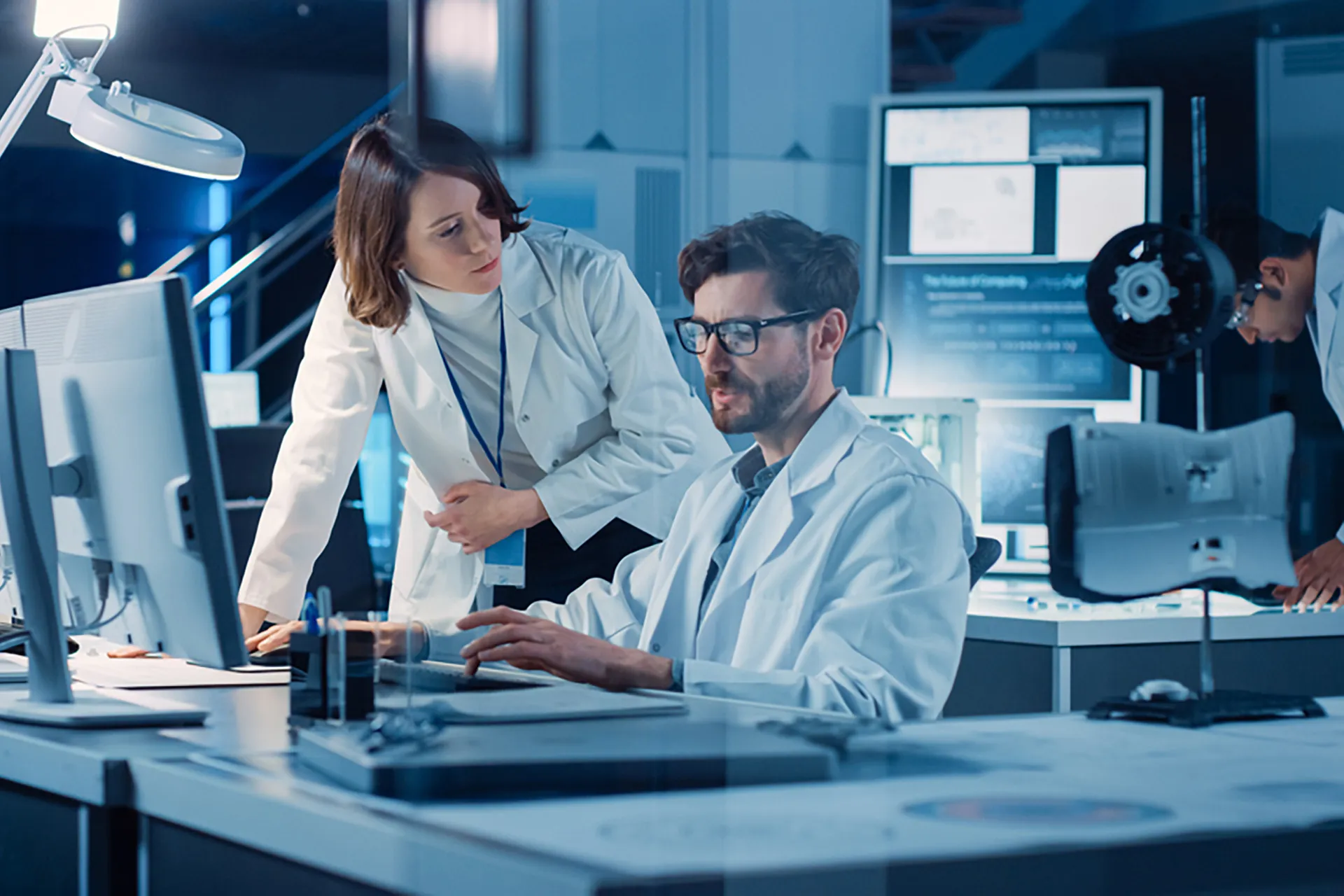 A male and female engineer in lab coats working at a computer.