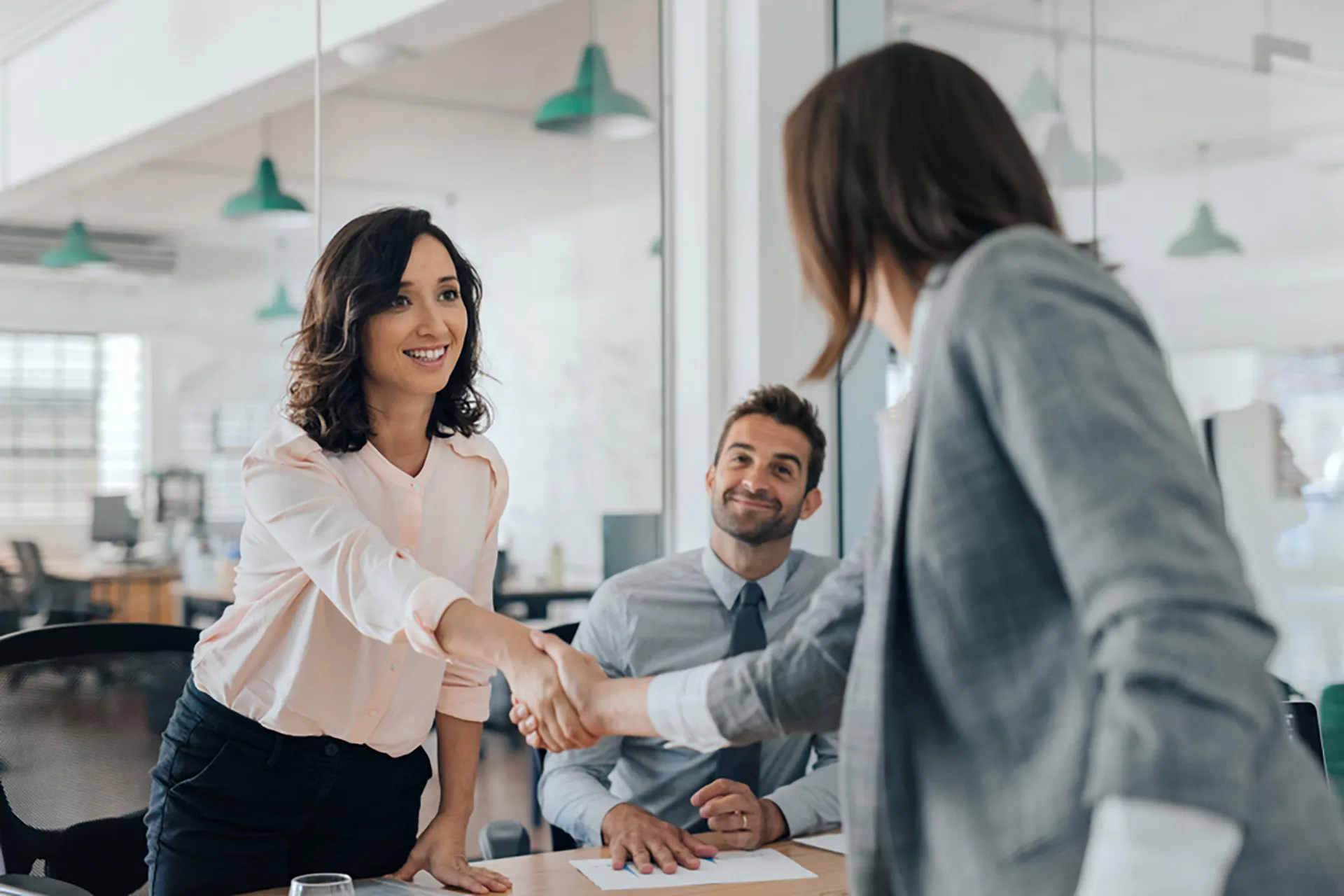 A woman confidently shaking hands with two individuals in a professional office setting.