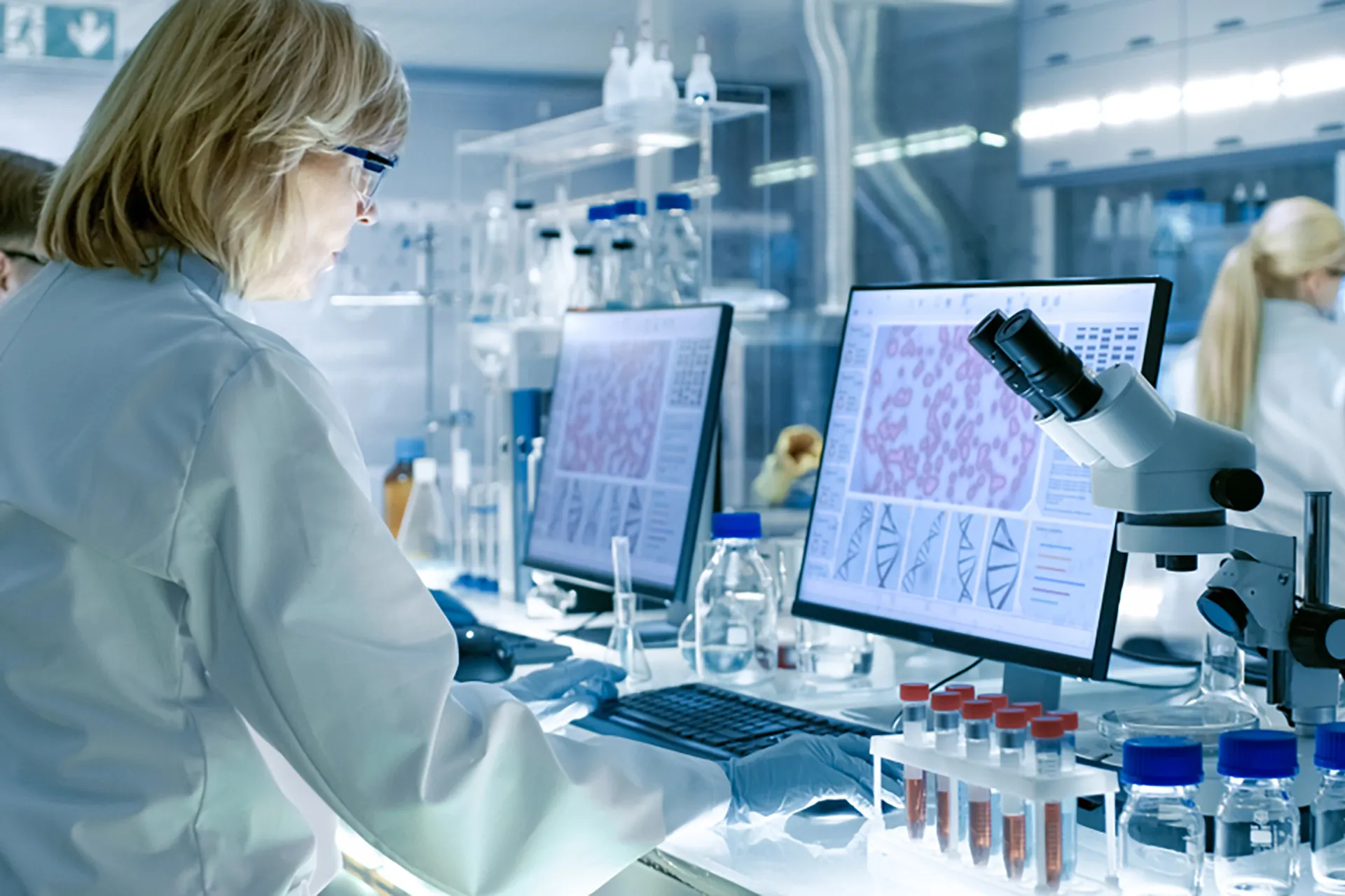 Rear view of a female scientist in a lab coat, focused on her computer screen, conducting research and analysis.