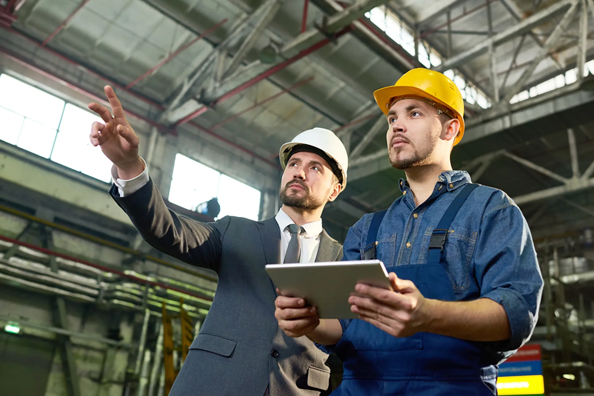 Two men in hard hats holding a tablet, discussing plans.