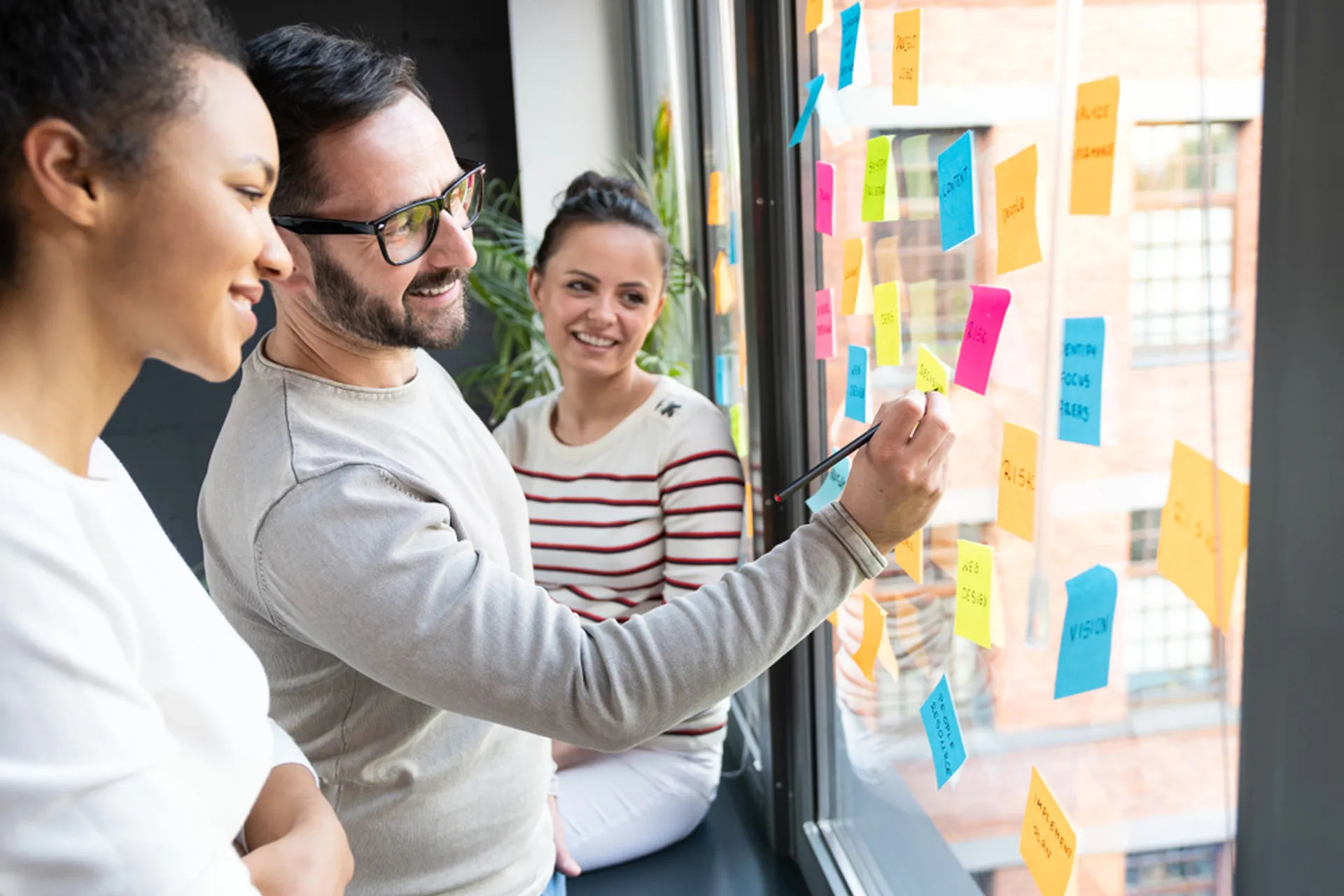 Three marketing professionals reviewing sticky notes on a window, engaged in a productive discussion.