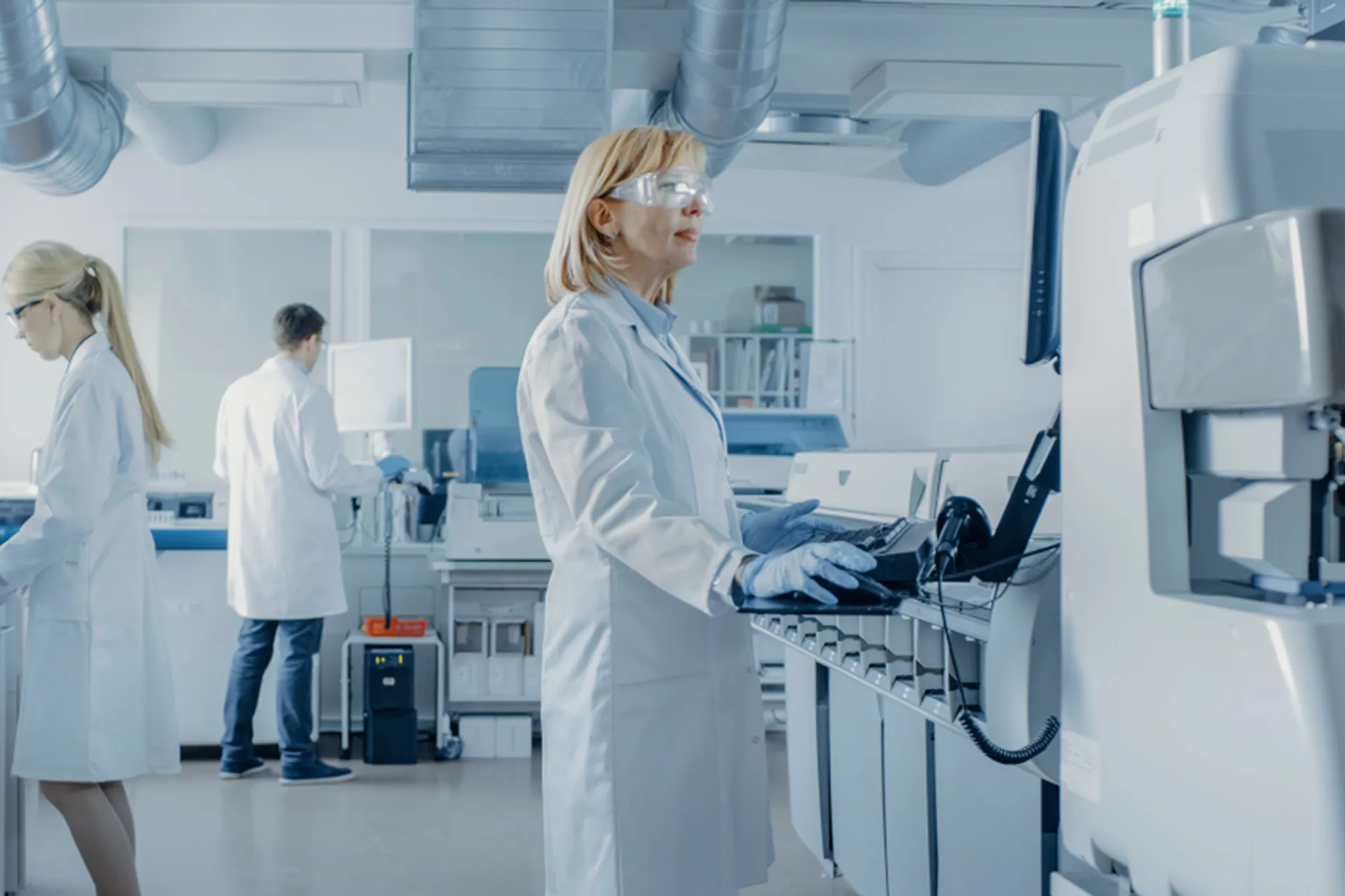 A woman in a lab coat focused on her computer screen, conducting research in a scientific laboratory.