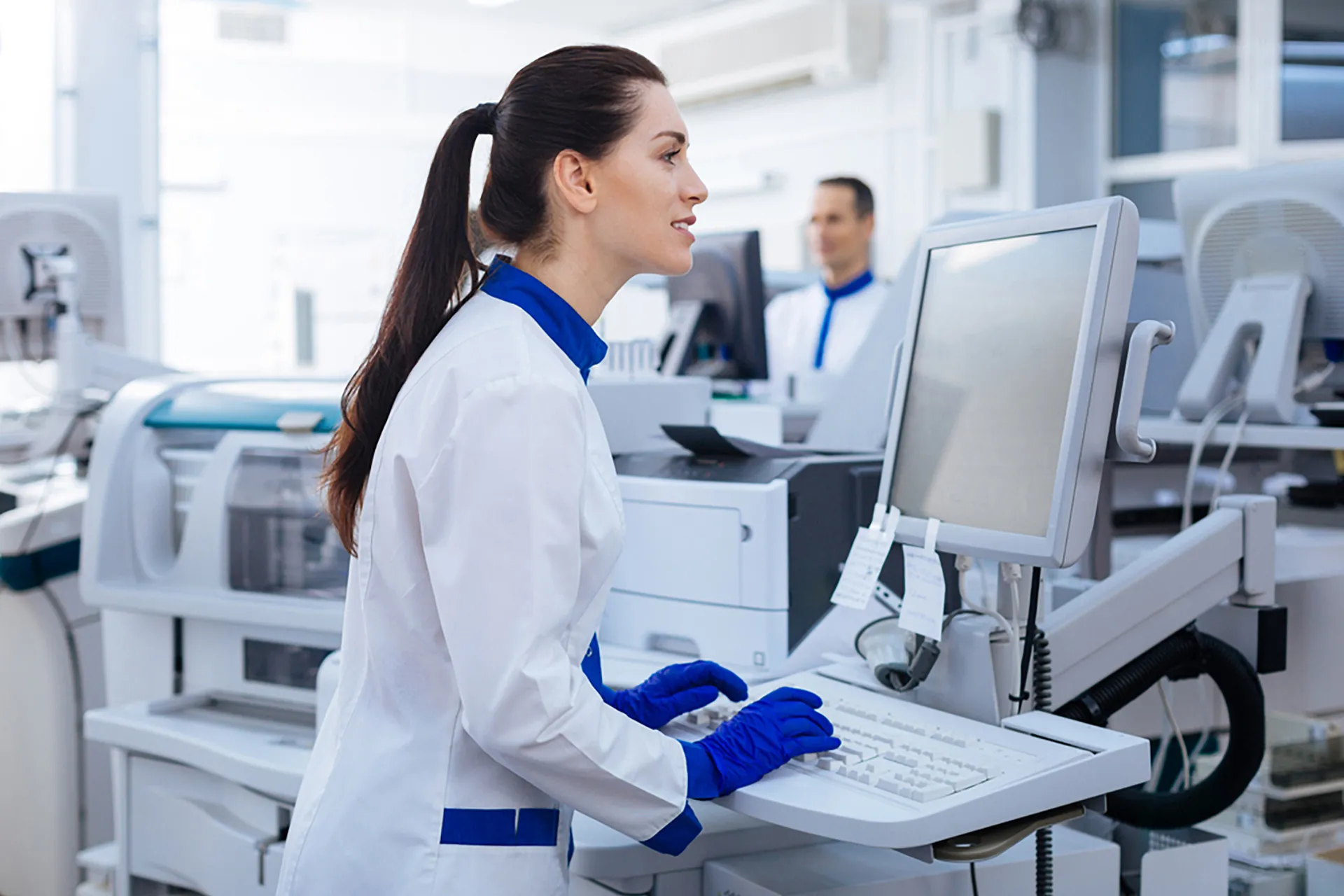 A female scientist in a lab coat is focused on her computer screen, conducting research and analysis.