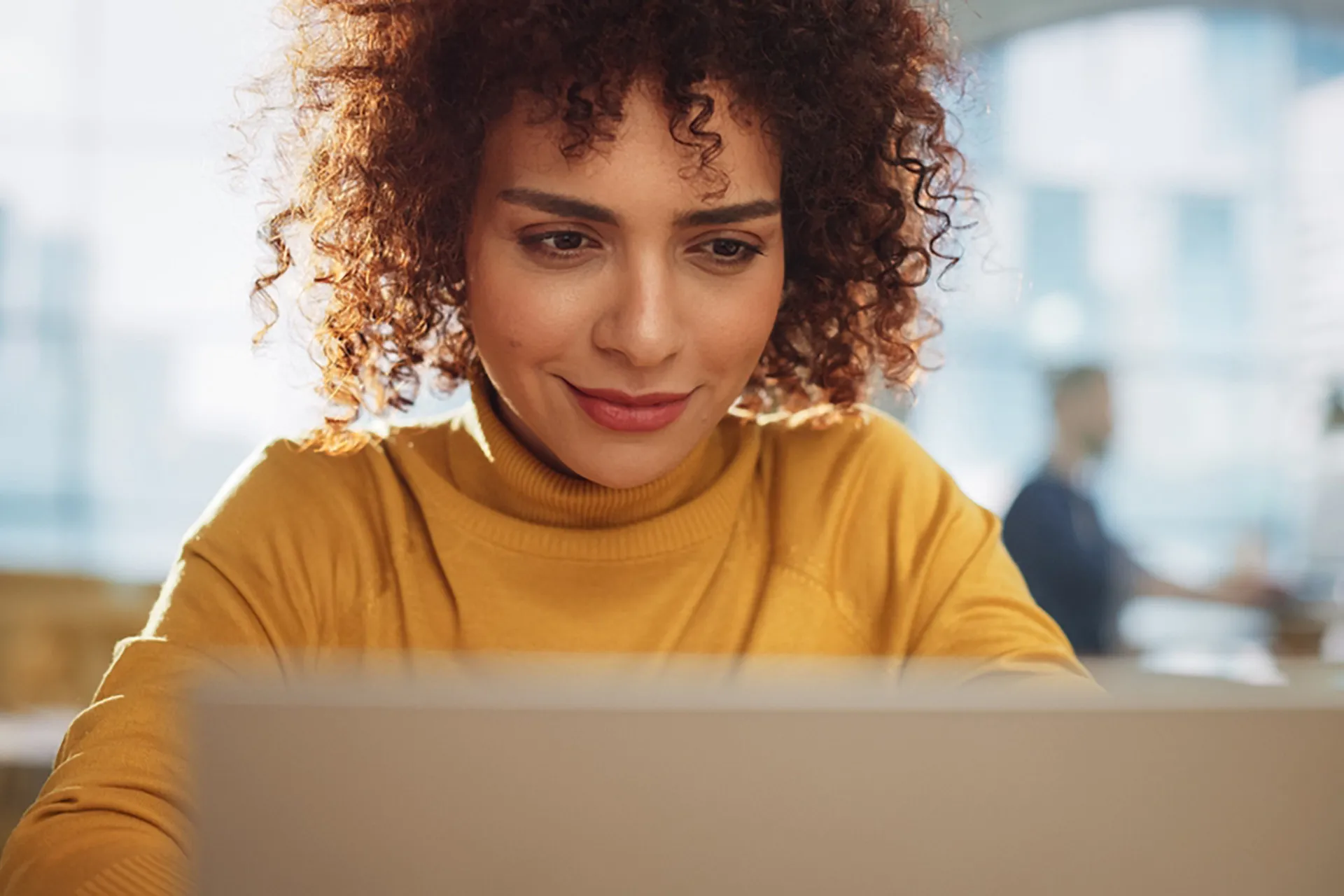 A woman with curly hair focused on her laptop screen, engrossed in her work.