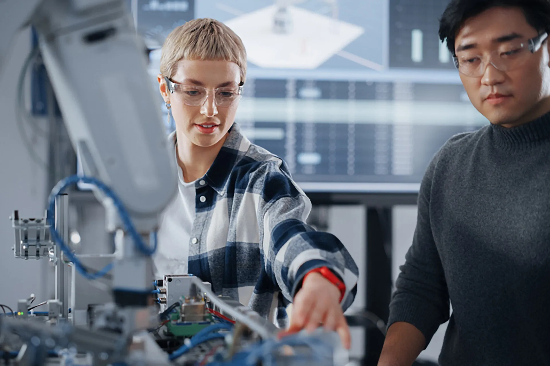  Two people wearing safety glasses, collaborating on a robot in an workshop environment.