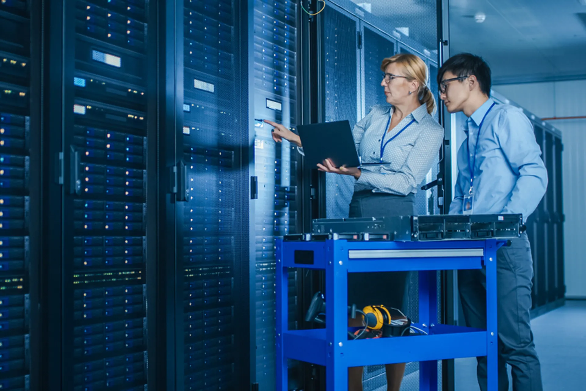 Two people in a server room, analysing data output on a computer screen.